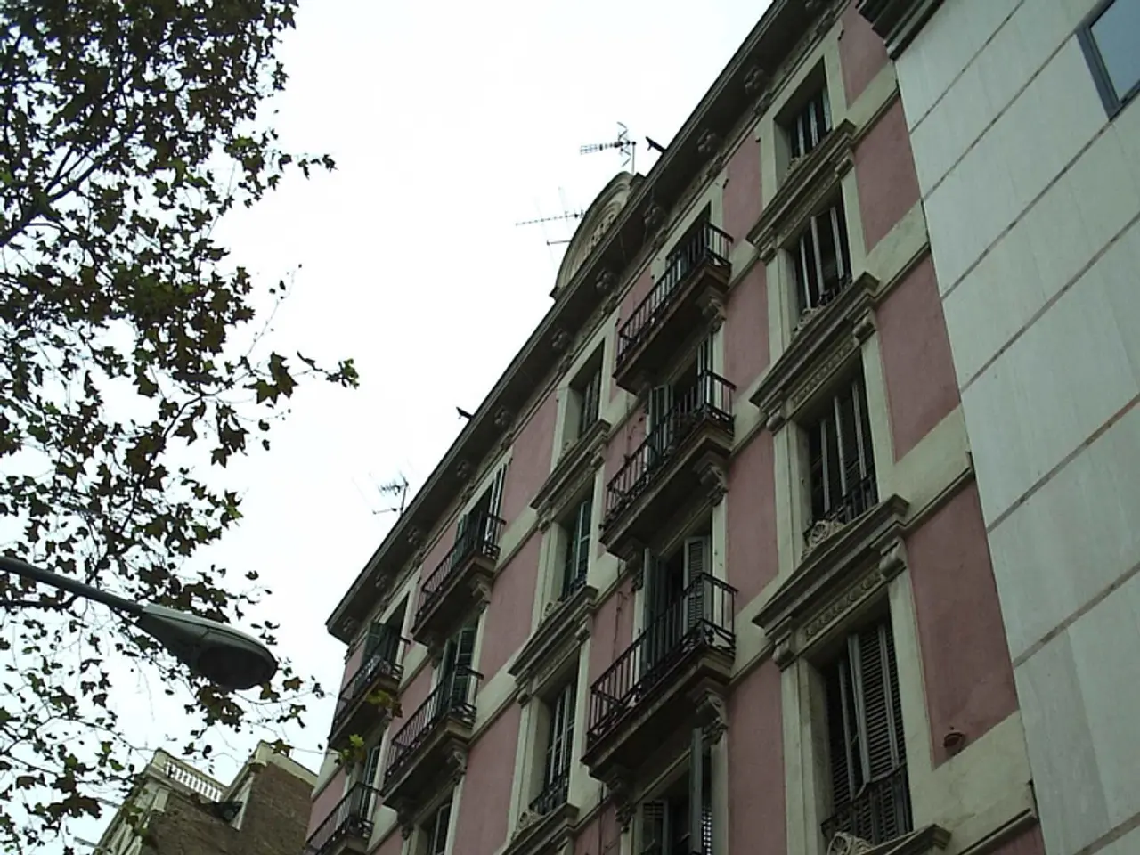 In this picture we can see buildings with many balcony windows and lights. Here we can see green...