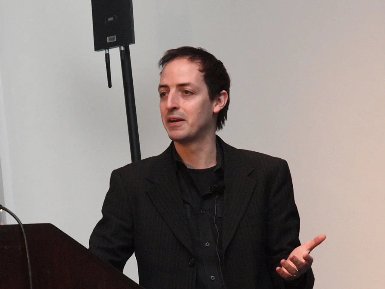 A man is standing wearing suit, these are bottles and cables, this is wall.