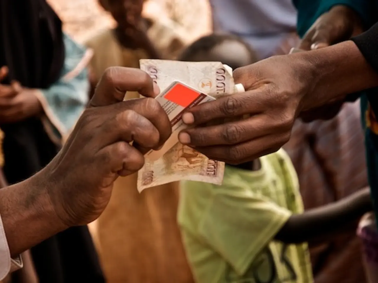 In this image there is a card and a money note in between the two hands. Both the persons on either...