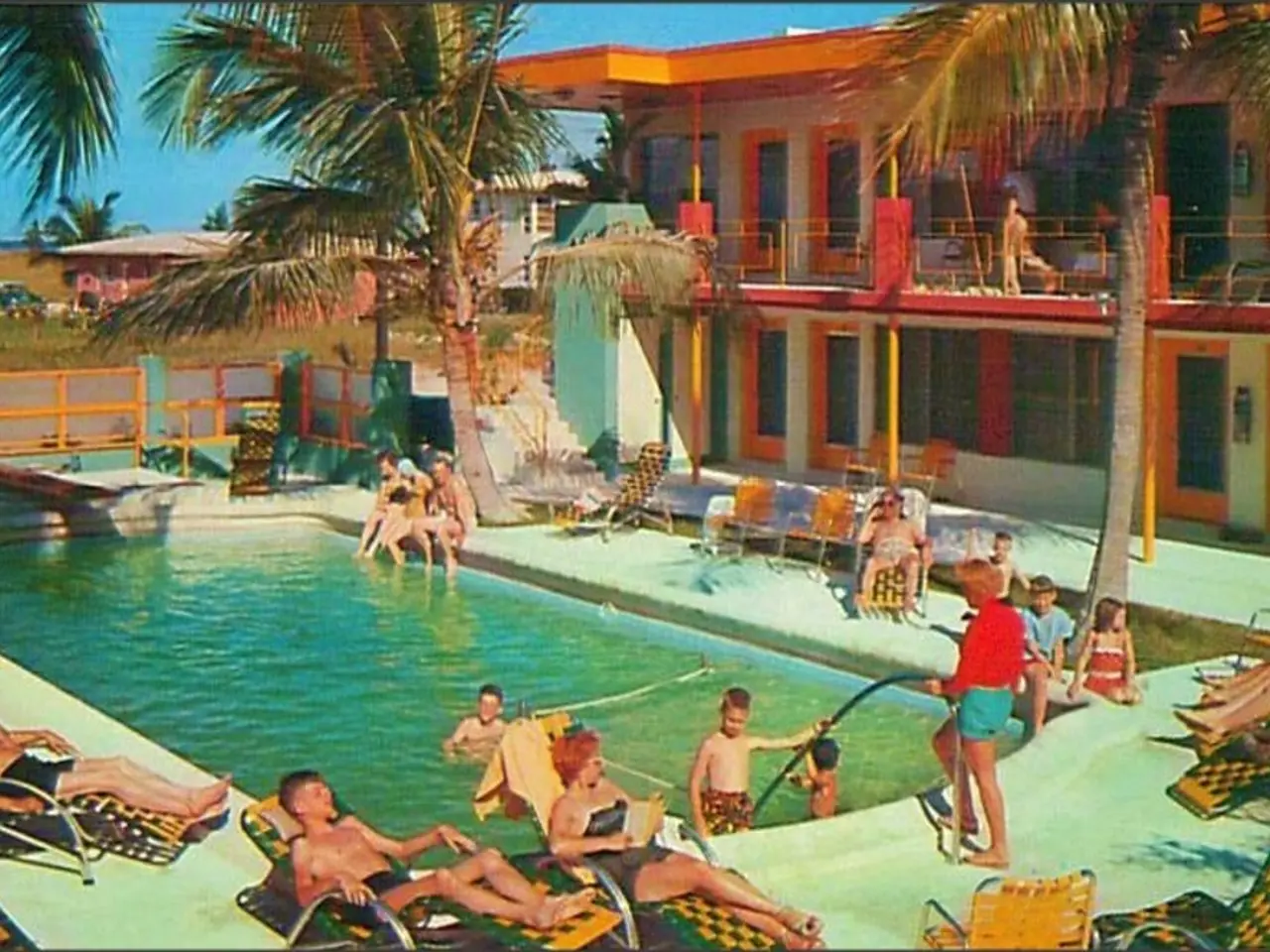 In the center of the image there is a swimming pool. There are people sitting on chairs. In the...