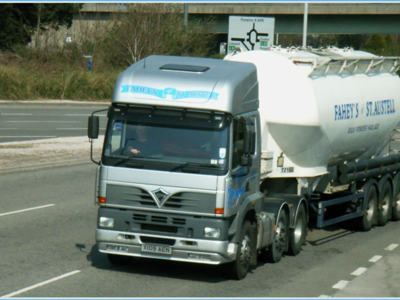 In this image there is a truck passing on the road, inside the truck there is a driver, on the...