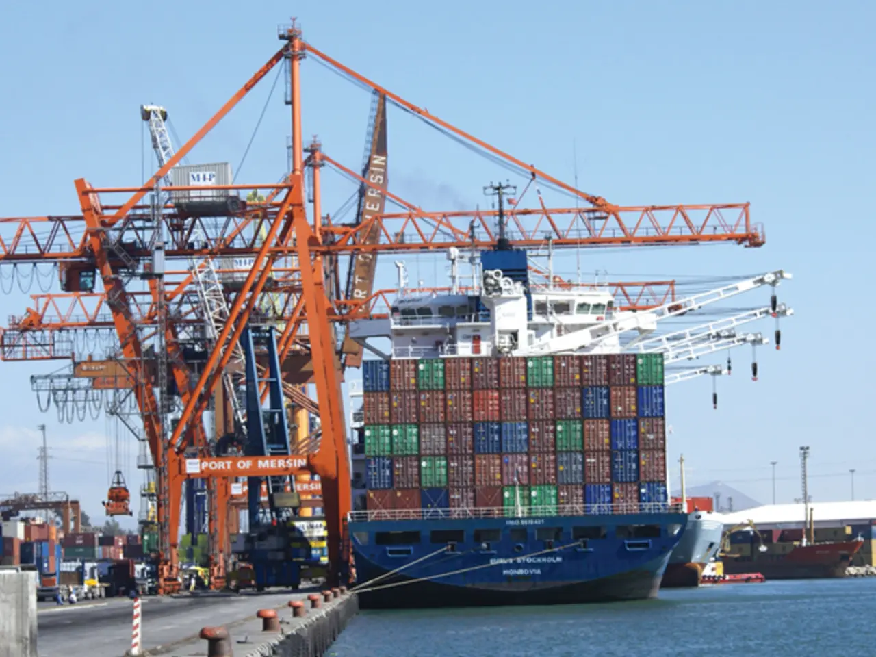 The image is taken from the port beside a sea,there are very big cranes and many goods on the...