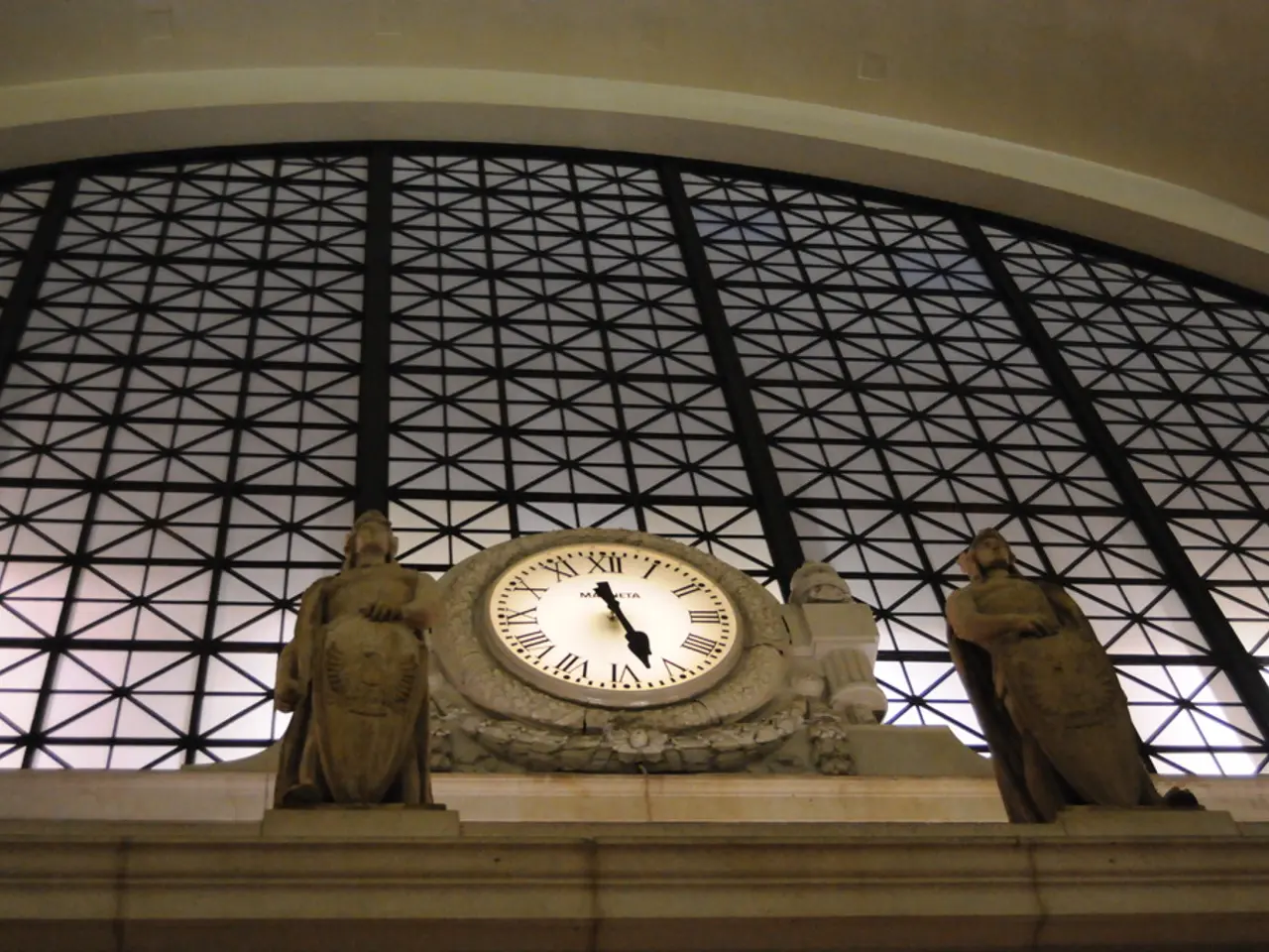 In this image there is a building and a clock is attached to it. There is a sculptures in the...
