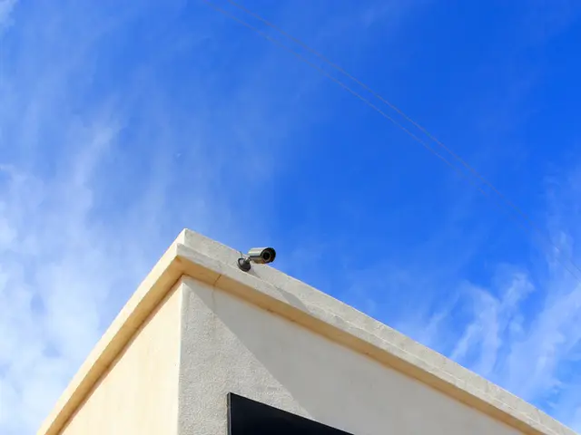 There is a name board on the wall of a building, which is having cc camera and glass doors. In the...