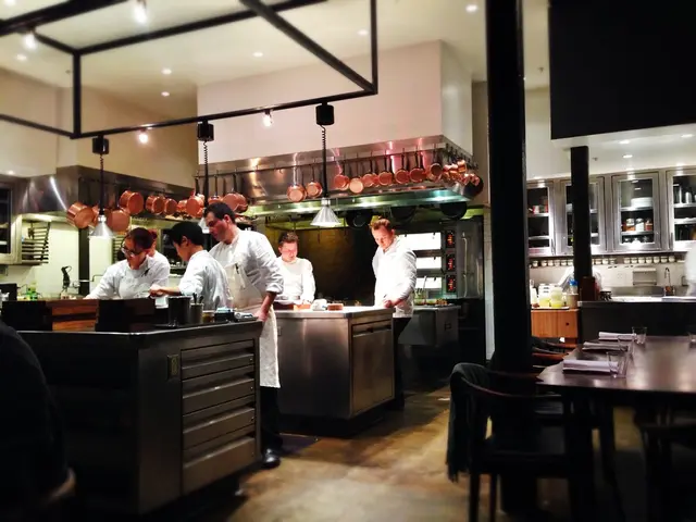 There are five persons who are working in the kitchen. This is a wooden table where a glass and...