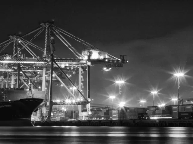 In this image there is a shipyard with metal structures, lamp posts, containers and ships.